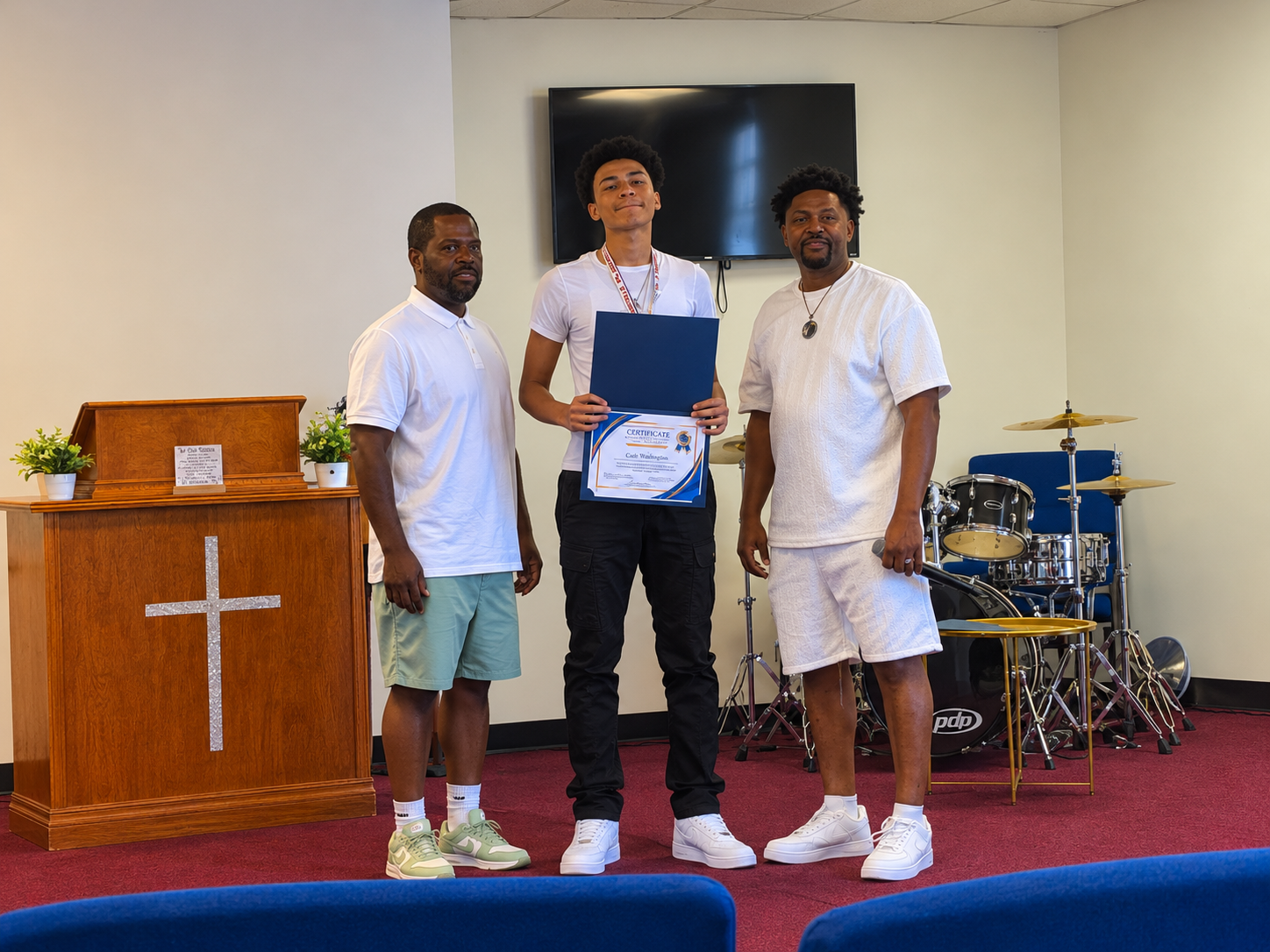 An alumnus holds his certificate of completion alongside two mentors